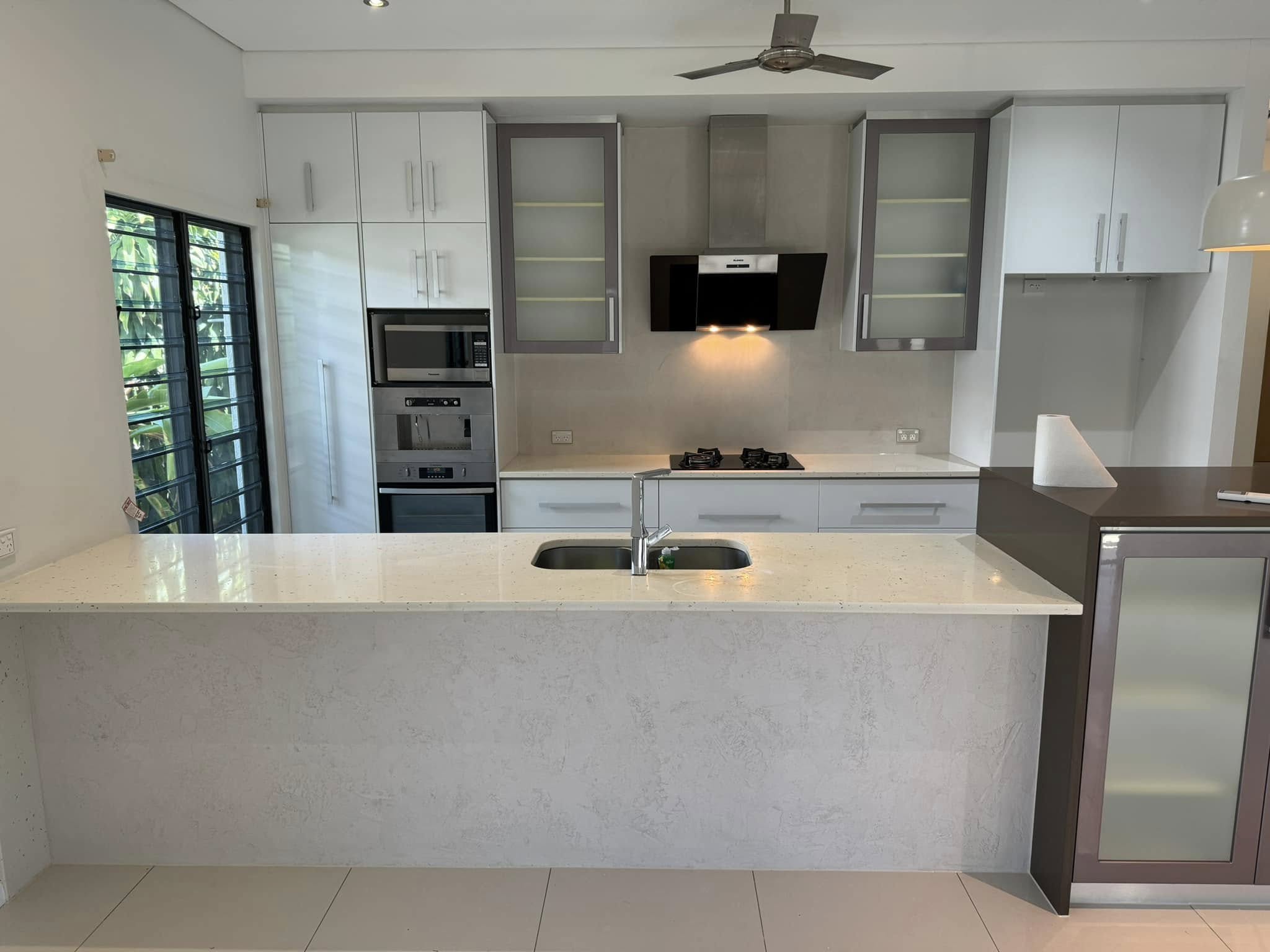 1-home-about1 Kitchen with white cabinets, a black range hood and a pale stone-look island bench