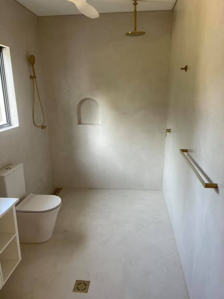 Walk-in shower with seamless beige walls and floor, brass fittings and a wall niche